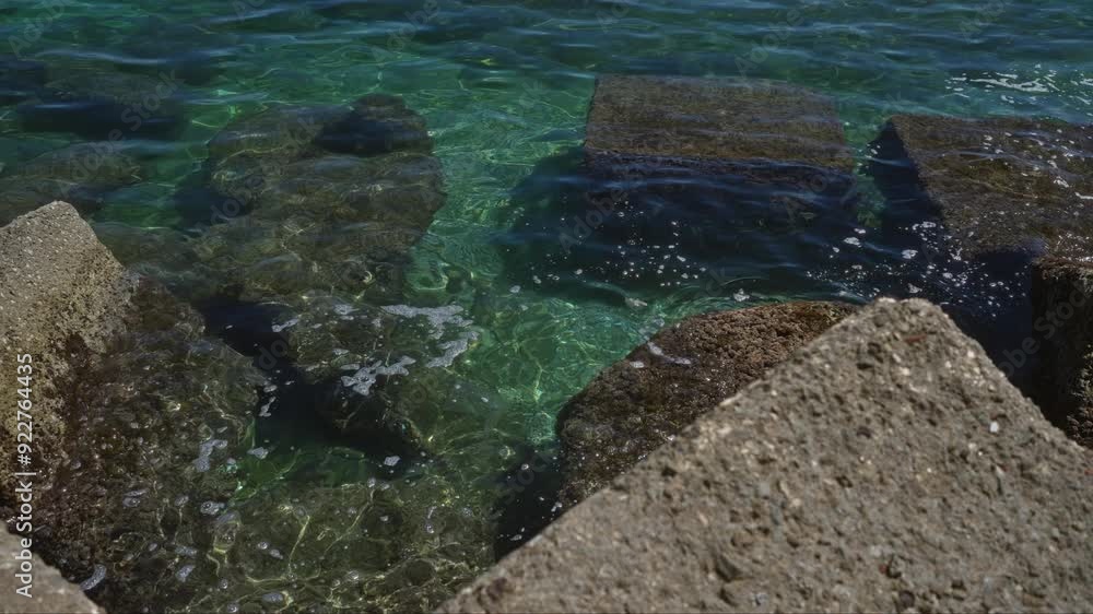 Clear ocean water with visible underwater rocks and concrete blocks, captured outdoors on a sunny day, illustrating marine textures and vibrant greenery. Clear ocean water with visible underwater rocks and concrete blocks, captured outdoors on a sunny day, illustrating marine textures and vibrant greenery.