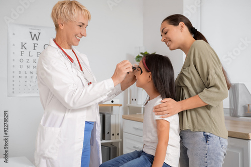 Female pediatrician putting ophthalmic trial frame on little girl and mother in clinic