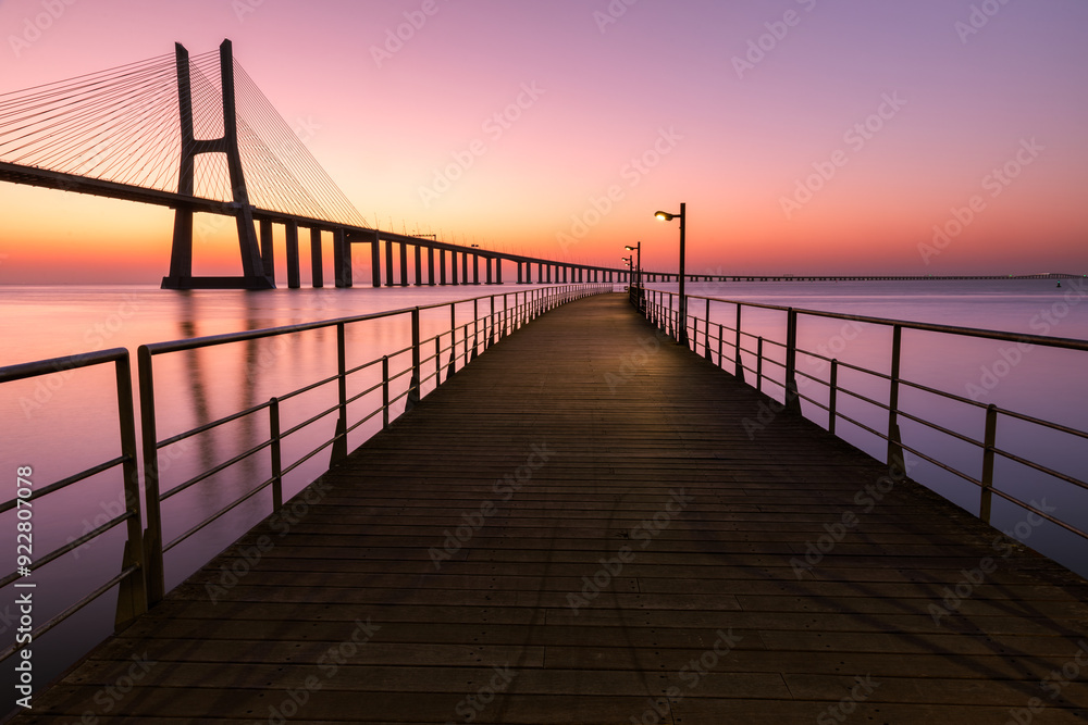 Fototapeta premium Pier. Path to the river. Dawn on the river with a large cable-stayed bridge. Vasco da Gama Bridge in Lisbon, Portugal 