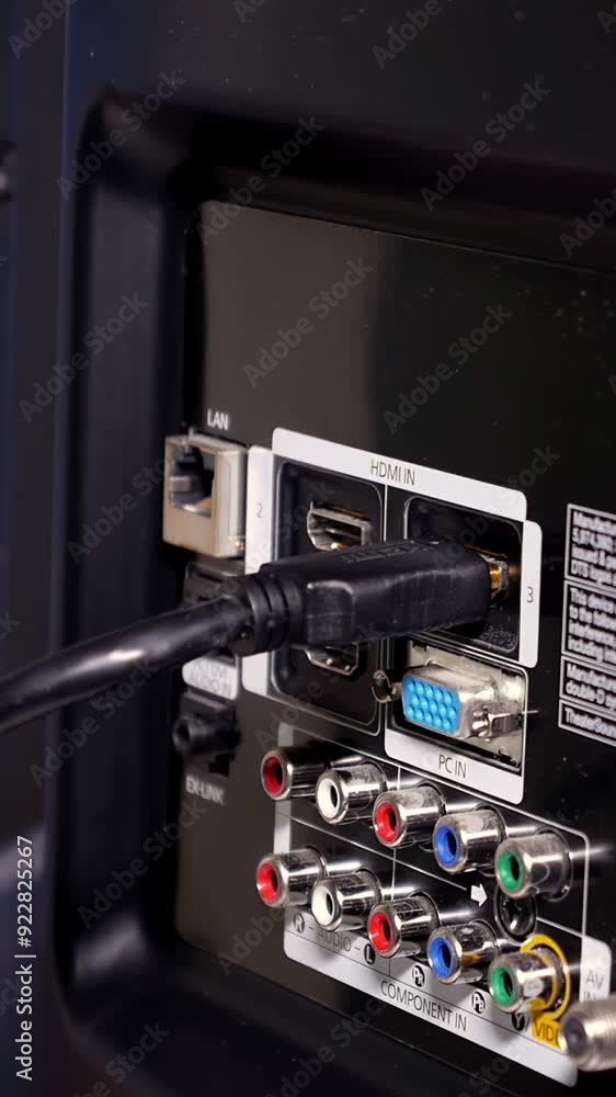 A vertical close-up shot of a cable installer plugging-in an HDMI cable to the back of a customer's television. A vertical close-up shot of a cable installer plugging-in an HDMI cable to the back of a customer's television.