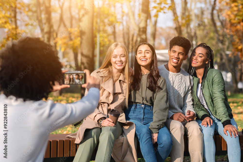Fototapeta premium Black guy teenager taking photo of his happy international friends in autumn public park