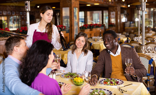 Wallpaper Mural Cheerful laughing adults enjoying friendly gathering over dinner in restaurant. People carefree chatting at table while young waitress serving them bottle of wine Torontodigital.ca