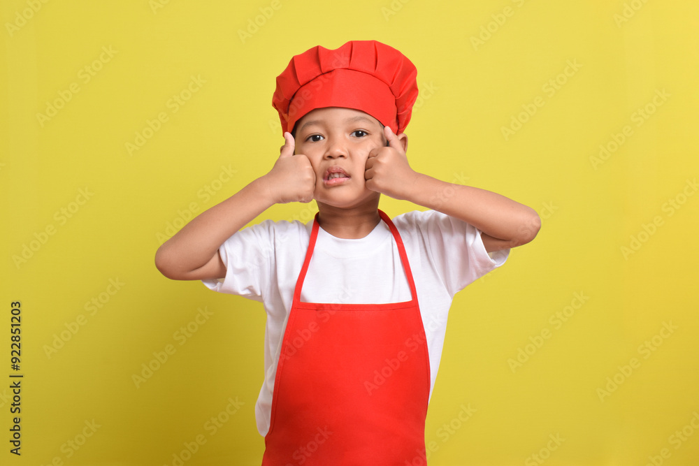 Cute little chef showing thumbs up isolated on yellow background. Asian boy wearing red apron and hat. Great little chef Cute little chef showing thumbs up isolated on yellow background. Asian boy wearing red apron and hat. Great little chef