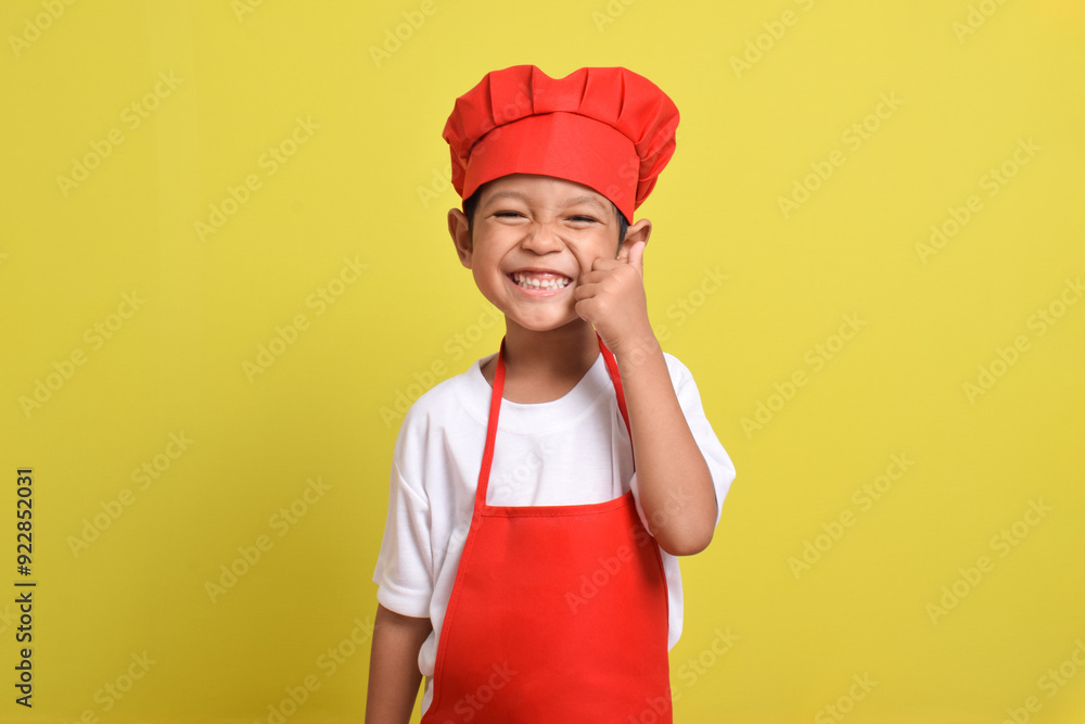Cute little chef showing thumbs up isolated on yellow background. Asian boy wearing red apron and hat. Great little chef Cute little chef showing thumbs up isolated on yellow background. Asian boy wearing red apron and hat. Great little chef