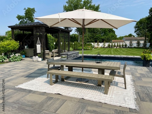 High-end outdoor living space, a backyard patio with pergola, outdoor rug,  tequila bar, dining set, couch, television, pool with waterfall, umbrella, fire pit and stunning grey patio. Modern vibe. photo