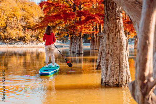 Woman paddle boarding on a lake with trees in warm morning light photo