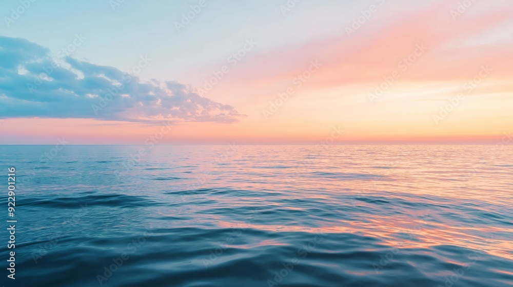Obraz premium Gentle waves reflecting a pastel sunset over calm waters at the coastline.