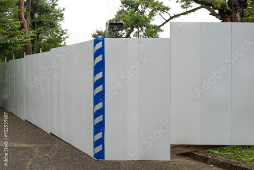 A white blank construction fence or barrier wall at a work site, with a striped soft pad running along the corner edge to warn and protect people from the sharp edge. Copy space for design photo