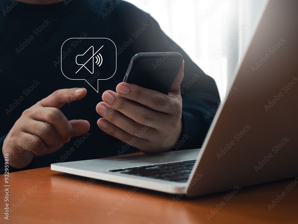 Silent mode concept. Silent or mute sound icon turn activated on appear in speech bubble while businessman holding mobile smart phone and working with laptop computer on table in office workplace.