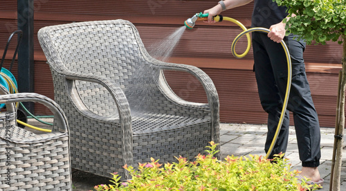 Anonymous cleaning, hose water washing wicker furniture from summer. Structures in backyard. Cleanliness and order. 