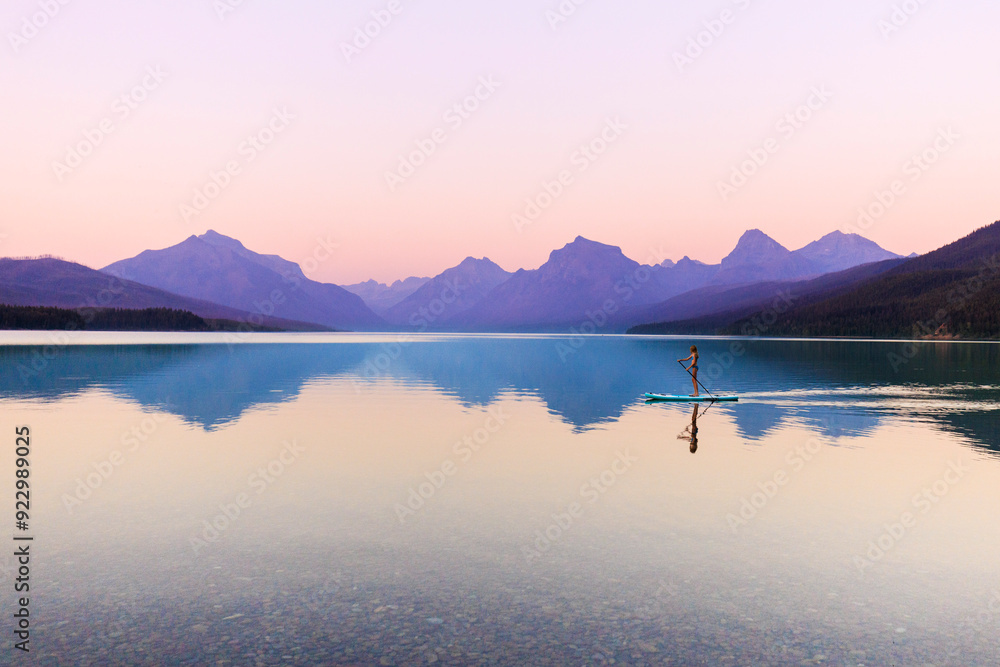 Fototapeta premium A woman paddle boards on Lake McDonald in Glacier National Park at sunset