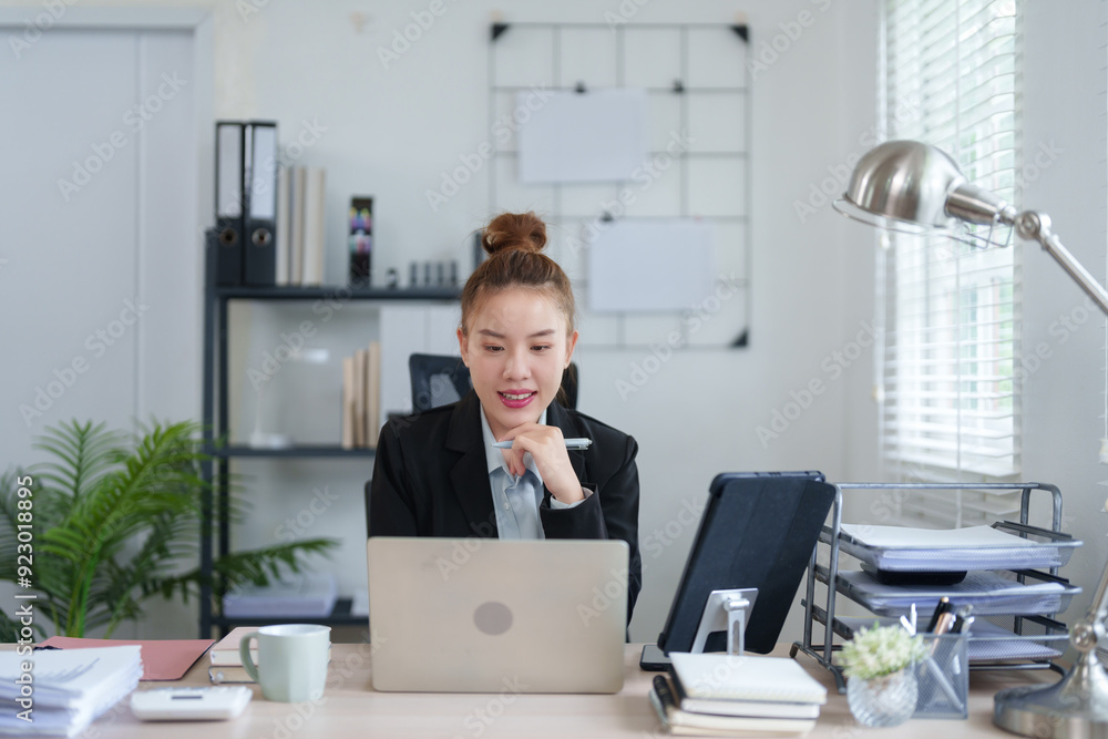 A professional woman in a black suit is sitting at her desk, concentrating on her work with a laptop, surrounded by files and office supplies, showing a focused work atmosphere A professional woman in a black suit is sitting at her desk, concentrating on her work with a laptop, surrounded by files and office supplies, showing a focused work atmosphere