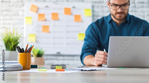 A focused man works on a laptop with stationery and post-it notes, showcasing productivity in a modern office environment.