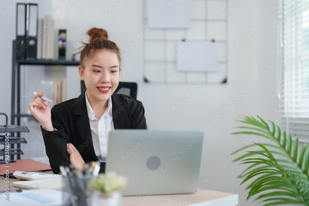 A confident businesswoman in a black suit is sitting at her desk, smiling as she engages in an online meeting, with notes and documents organized on the table in a modern office A confident businesswoman in a black suit is sitting at her desk, smiling as she engages in an online meeting, with notes and documents organized on the table in a modern office