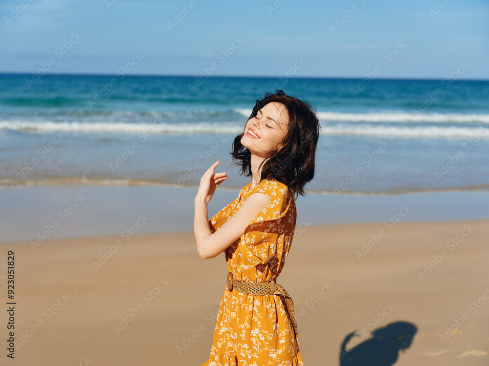Woman in a vibrant yellow dress joyfully raising her arms on the sandy beach shore Woman in a vibrant yellow dress joyfully raising her arms on the sandy beach shore