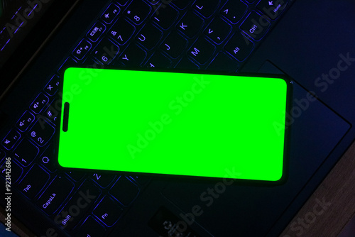 selective focus cellphone or handphone or smartphone with green screen lying on a dark laptop keyboard