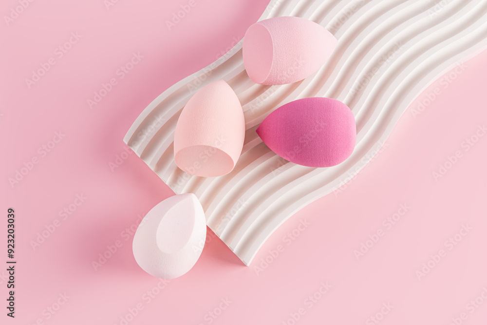 Fototapeta premium Four beauty blenders sponges in pink shades on a white embossed catwalk and a pink background. top view. Care and beauty concept. Makeup tool.