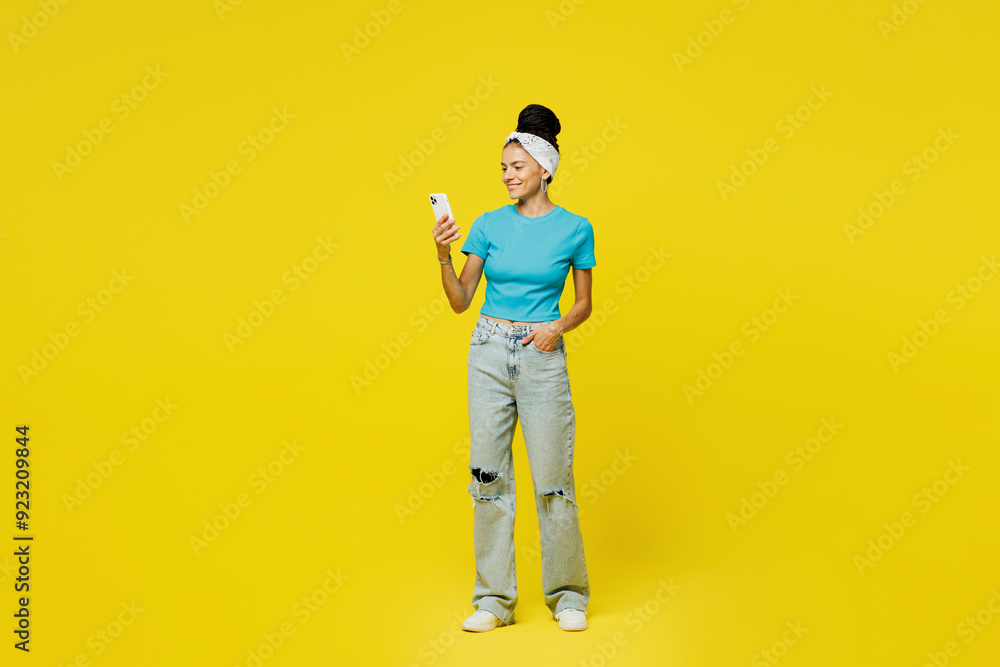 Fototapeta premium Full body young Latin woman wears blue top t-shirt headband casual clothes hold in hand use mobile cell phone typing message chat online isolated on plain yellow background studio. Lifestyle concept.