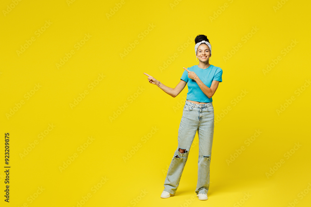 Fototapeta premium Full body young smiling happy fun Latin woman she wears blue top t-shirt headband casual clothes point index finger aside on area mock up isolated on plain yellow background studio. Lifestyle concept.
