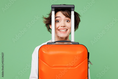 Close up traveler cheerful woman wears casual clothes hold orange suitcase bag look camera isolated on plain green background. Tourist travel abroad in free time rest getaway. Air flight trip concept. #923214227