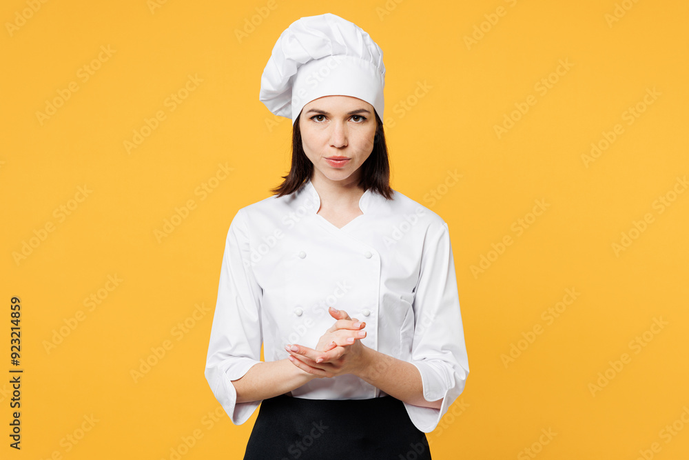 Young angry serious sad confident indignant chef cook baker woman she wear white shirt black apron uniform toque chefs hat look camera isolated on plain yellow background studio. Cooking food concept. Young angry serious sad confident indignant chef cook baker woman she wear white shirt black apron uniform toque chefs hat look camera isolated on plain yellow background studio. Cooking food concept.