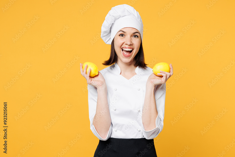 Young surprised shocked chef cook baker woman wear white shirt black apron uniform toque chefs hat hold in hand two lemons look camera isolated on plain yellow background studio. Cooking food concept. Young surprised shocked chef cook baker woman wear white shirt black apron uniform toque chefs hat hold in hand two lemons look camera isolated on plain yellow background studio. Cooking food concept.