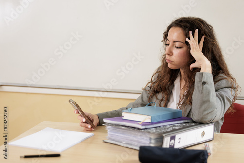 Overwhelmed and tired businesswoman looking for a client's phone number on her cell phone. Displeased teacher writing a message or email to parents about a problem with their son or daughter.