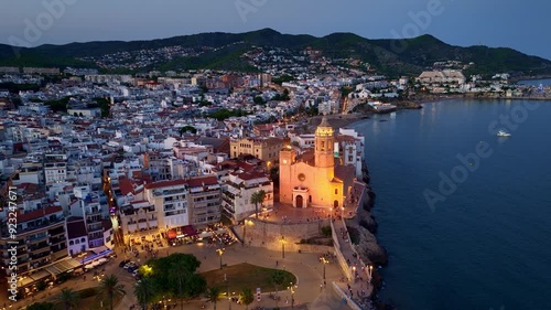 Night aerial view of Costa Brava in Spain, coastal Spanish village of Sitges drone view in the evening, mediterranean holiday resort in Spain with medieval church at night