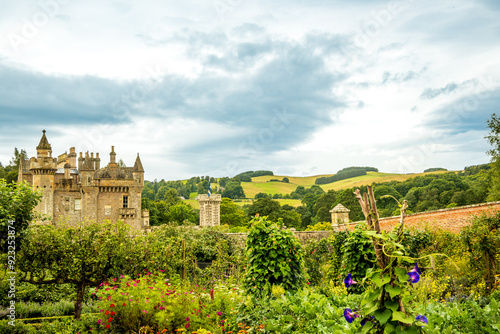 Romantic castle style building seen from a garden with apple trees and flowering plants with green hills and clouds in background shot Abbotsford Lothian Region Scotland room for text photo