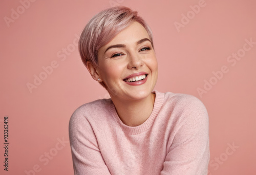 A vibrant portrait of a woman with short pink hair and a bright, genuine smile, set against a matching pink background that accentuates her cheerful and confident appearance.