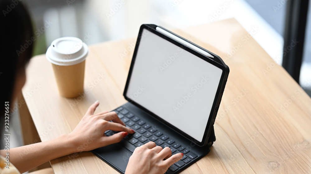 Close up image of hands typing on a black keyboard of digital tablet at wooden table with a cup of coffee Close up image of hands typing on a black keyboard of digital tablet at wooden table with a cup of coffee