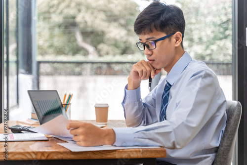 Young businessman working on his project in his office checking business result data from the printed sheets and his laptop computer