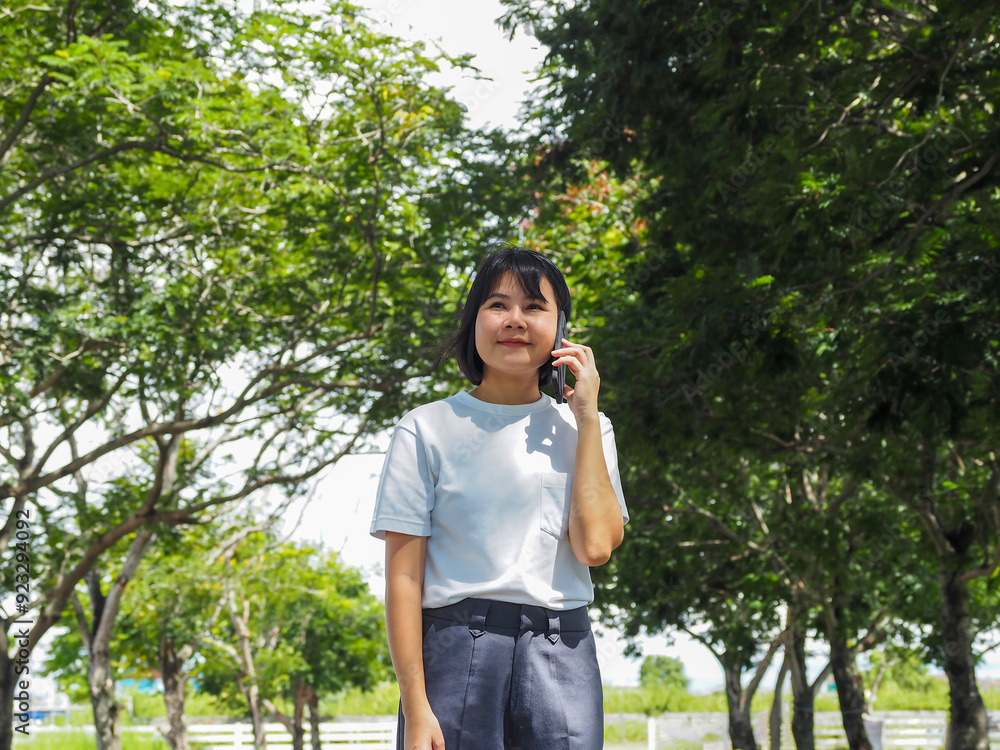 Asian businesswoman in white shirt walking and talking on the phone in public outdoor Asian businesswoman in white shirt walking and talking on the phone in public outdoor