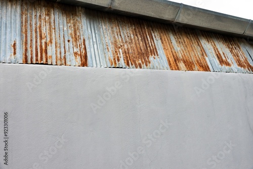 A rusted metal roof with a white wall behind it. The roof is old and has a lot of rust on it