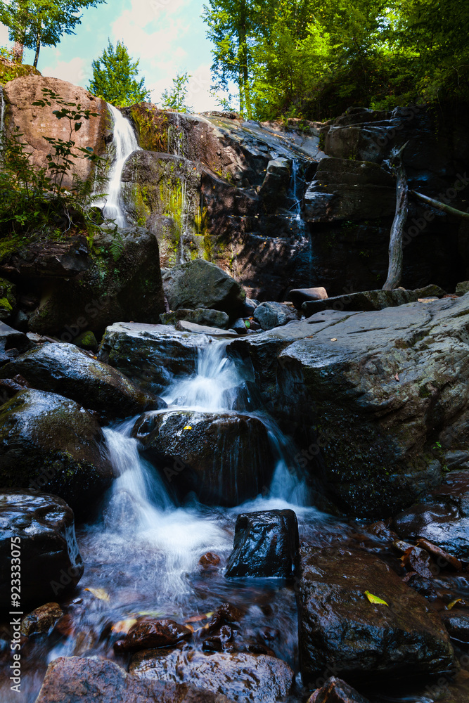 A captivating image of a serene waterfall cascading down a rocky cliff surrounded by lush greenery. The water flows gently over the dark rocks, creating a peaceful and tranquil scene in a forested are A captivating image of a serene waterfall cascading down a rocky cliff surrounded by lush greenery. The water flows gently over the dark rocks, creating a peaceful and tranquil scene in a forested are