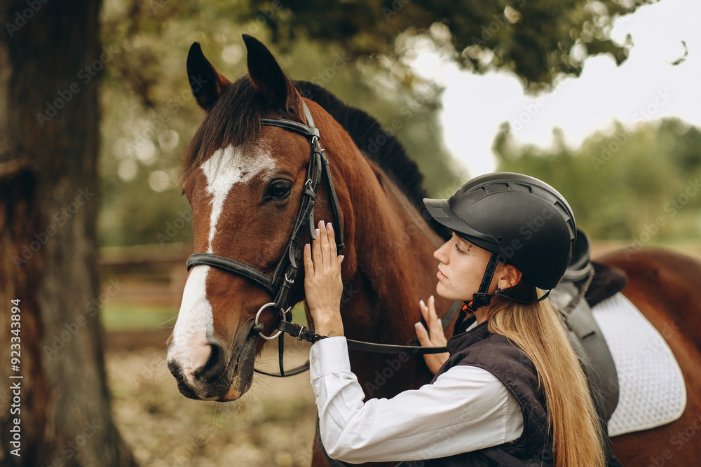 Obraz premium A young female equestrian stands near her horse and prepares for a competition.
