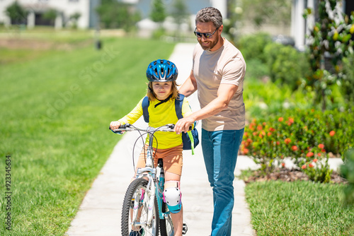 Fathers day. Boy learning to ride a bicycle with his father in park on summer day. Father teaching his son cycling on bike. Father learn little son to ride a bicycle. Father support kid. Happy Fathers