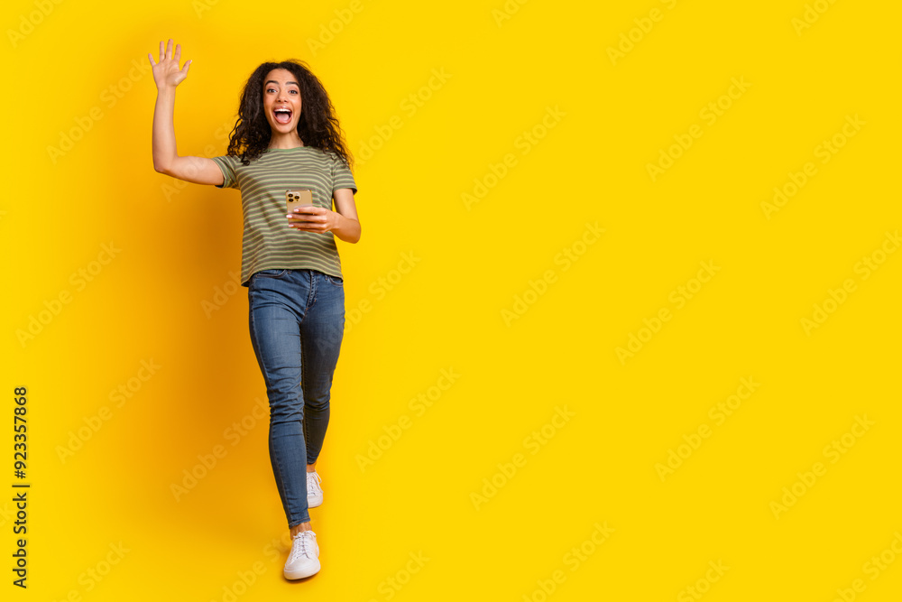 Full size photo of pleasant nice girl dressed t-shirt look at smartphone waving palm near empty space isolated on yellow color background Full size photo of pleasant nice girl dressed t-shirt look at smartphone waving palm near empty space isolated on yellow color background