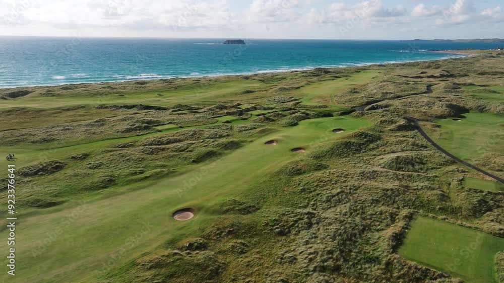 Drone flies over green rolling fairway of Ireland links golf course along coastline with blue waves crashing Drone flies over green rolling fairway of Ireland links golf course along coastline with blue waves crashing
