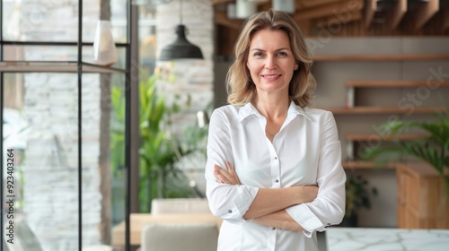 Confident businesswoman with crossed arms smiling in modern office, facing camera, embodying success in professional attire with sleek hairstyle.