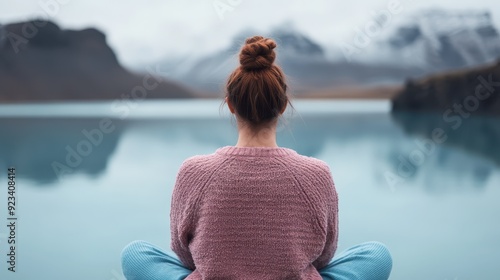 A person sits cross-legged meditating by the lake, with mountains and a serene landscape in the background. The composition emphasizes tranquility and contemplation. photo