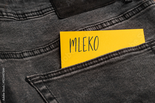 Yellow card with a handwritten inscription "Mleko", inserted into the pocket of gray pants jeasnow (selective focus), translation: Milk