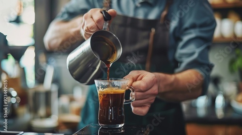 A focused barista carefully pouring coffee into a clear glass cup, emphasizing the careful attention to detail and care in every drink prepared.