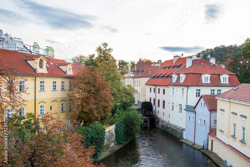 Narrow canal with ancient water-mill in among colorful houses with red roofs and autumn trees in Prague, Czech Republic. photo