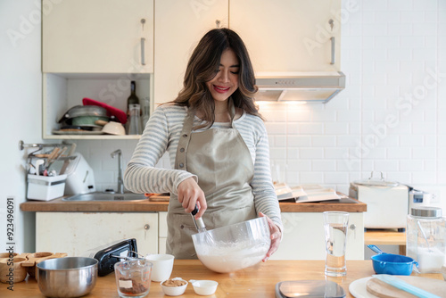 Young Woman Baking in a Modern Kitchen with Wooden Countertops and White Cabinets, Mixing Ingredients in a Bowl