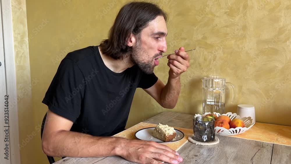 Man eating a slice of cake, then drinking from a mug in a cozy kitchen with fruits on the table. Morning routine in a casual setting