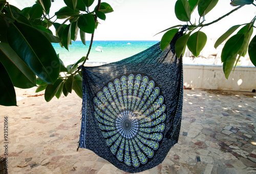 Pareo with blue designs hanging from the branches of a ficus plant, against a blue/green sea background.