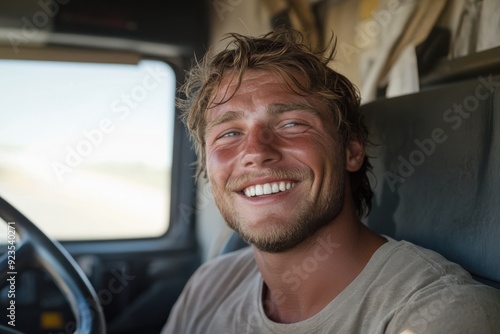 A young man with a wide smile, sitting in the driver's seat of a truck, capturing a moment of contentment and readiness for a journey on a sunny day.