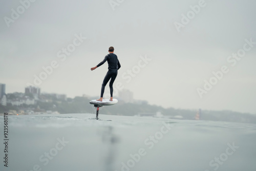 A young man in a wetsuit rides in the sea above the water on an electric powered hydrofoil board, efoil, e-foil, foil drive, hybrid foil. photo