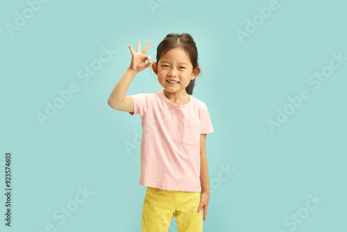 Isolated portrait of Joyful Asian Child Gesturing OK Sign standing over blue background with a free copy space